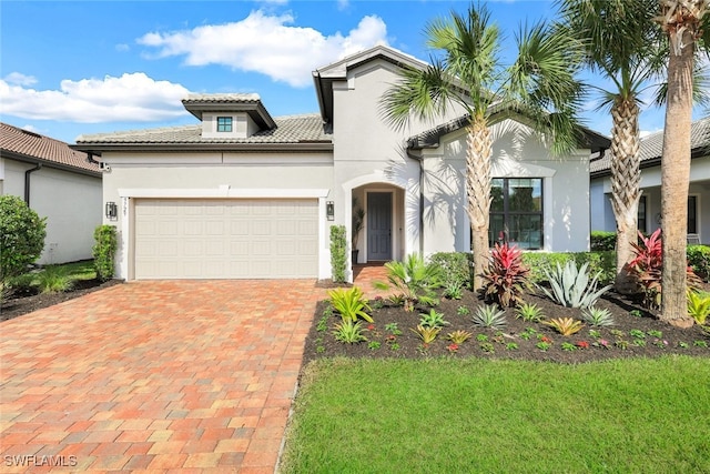 mediterranean / spanish-style home featuring decorative driveway, a tiled roof, an attached garage, and stucco siding