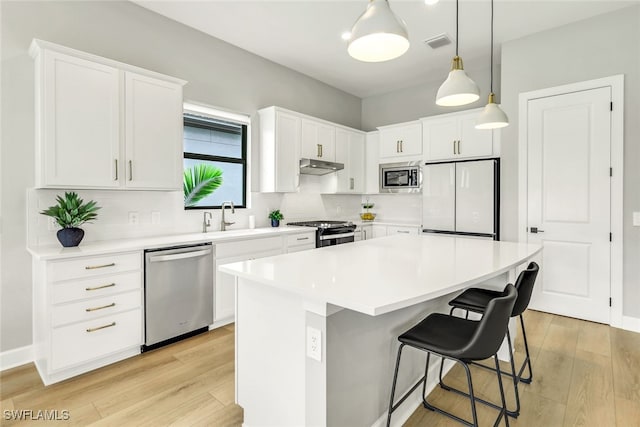 kitchen featuring white cabinets, under cabinet range hood, stainless steel appliances, and a sink