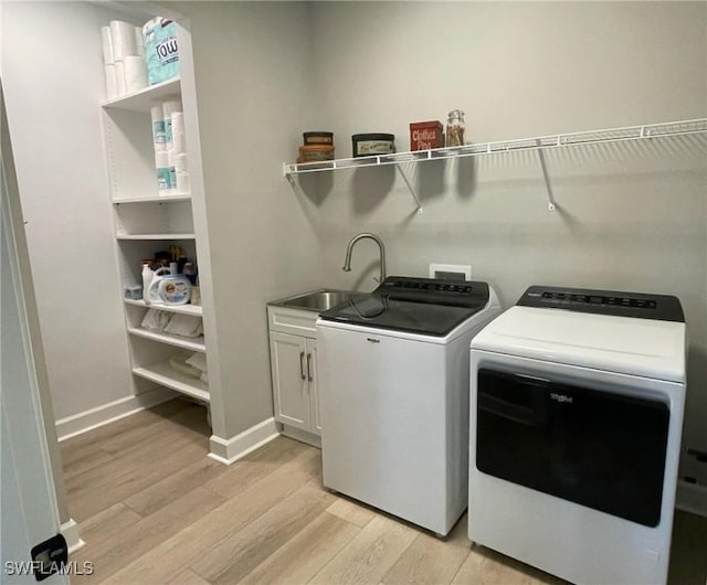 laundry room with light wood-style flooring, separate washer and dryer, a sink, baseboards, and cabinet space