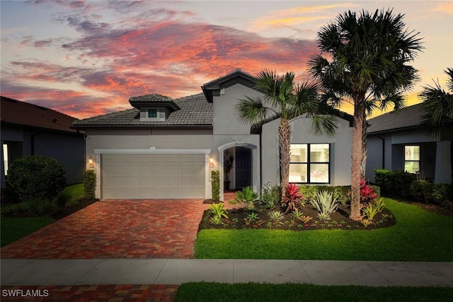 mediterranean / spanish house featuring a garage, decorative driveway, a tiled roof, and stucco siding