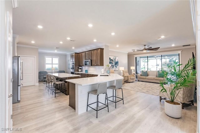 kitchen with crown molding, appliances with stainless steel finishes, a breakfast bar, and dark brown cabinetry