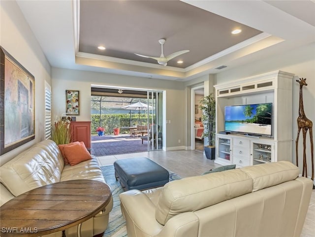 tiled living room with ceiling fan, ornamental molding, and a tray ceiling