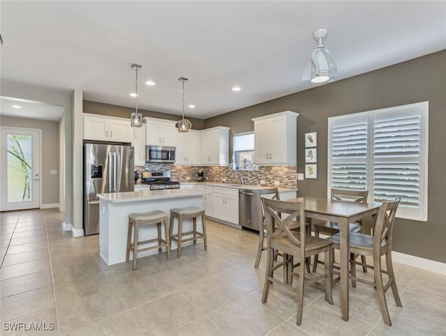 kitchen with appliances with stainless steel finishes, white cabinetry, hanging light fixtures, a kitchen island, and decorative backsplash