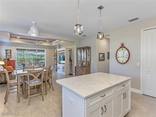 kitchen featuring decorative light fixtures, white cabinetry, a center island, light stone counters, and a raised ceiling