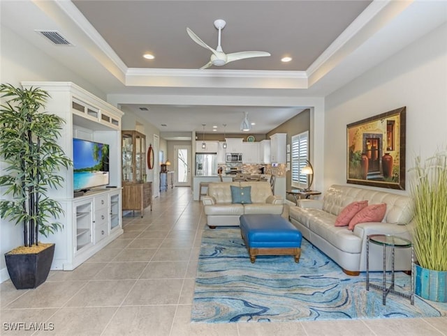 tiled living room with ceiling fan, ornamental molding, and a tray ceiling