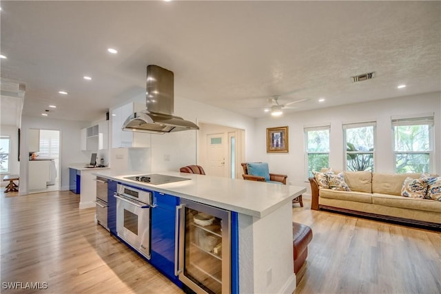 kitchen featuring island exhaust hood, black electric stovetop, light countertops, stainless steel oven, and beverage cooler