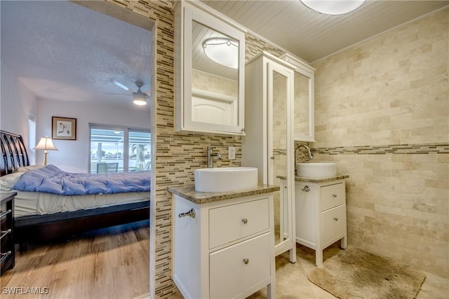 ensuite bathroom with connected bathroom, two vanities, a sink, and tile walls