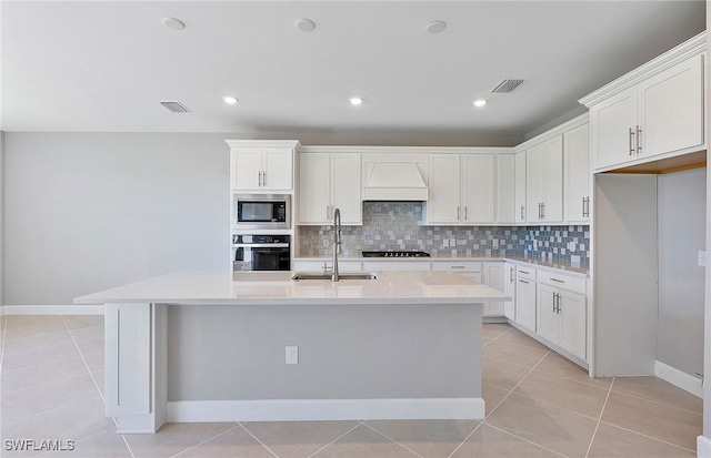 kitchen featuring built in microwave, sink, a kitchen island with sink, and white cabinets