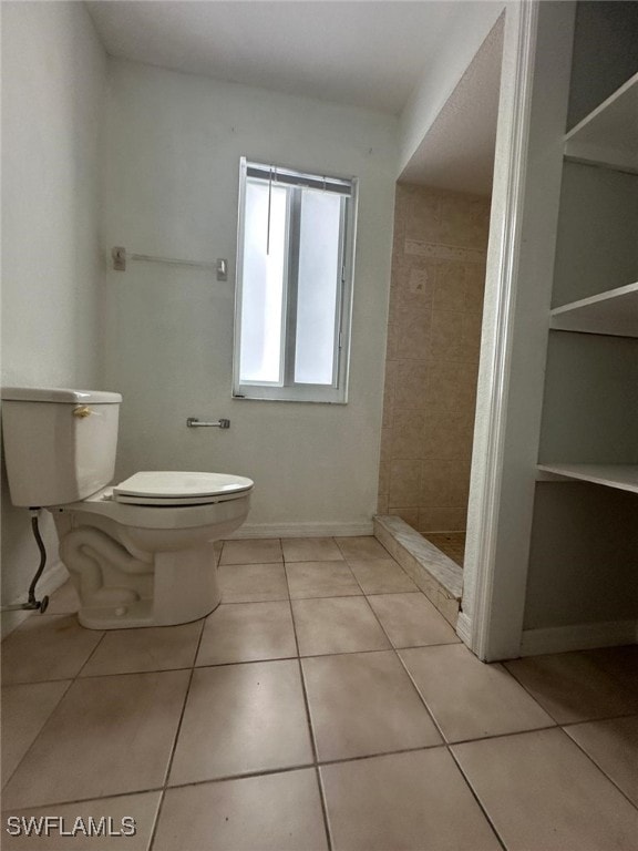 bathroom with tile patterned flooring, a tile shower, and toilet