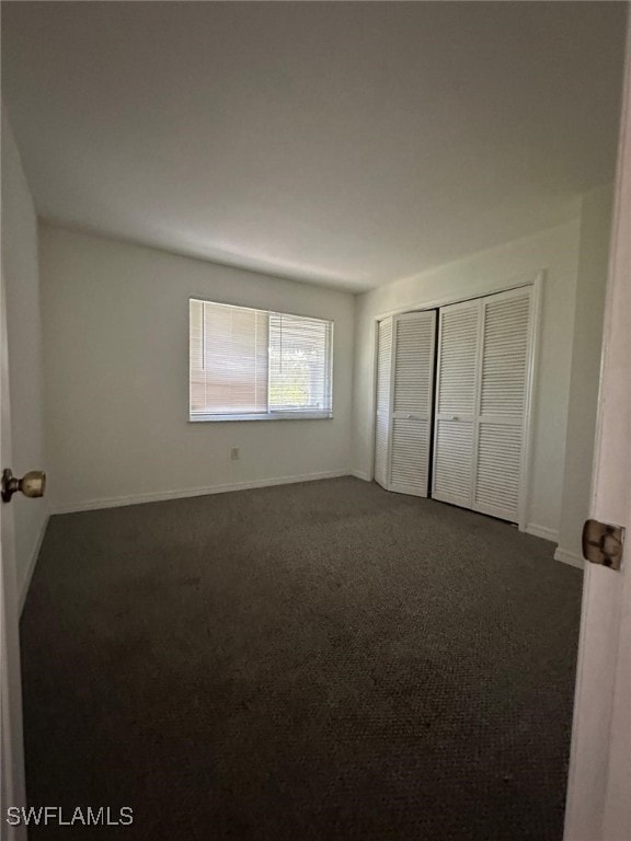 unfurnished bedroom with dark colored carpet and a closet