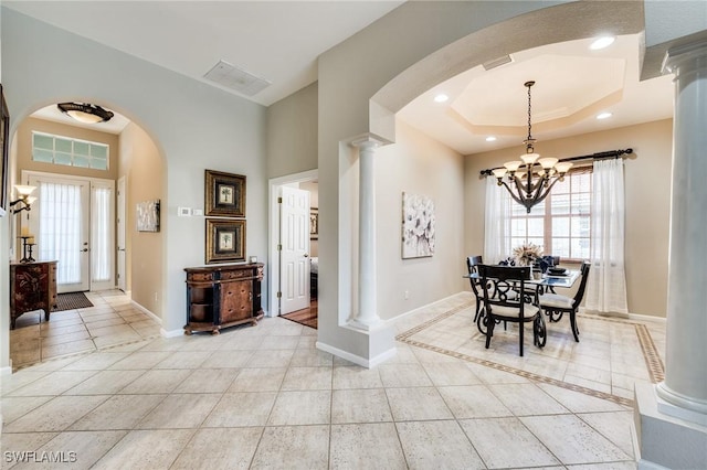 dining room with a notable chandelier, light tile patterned floors, a tray ceiling, and decorative columns