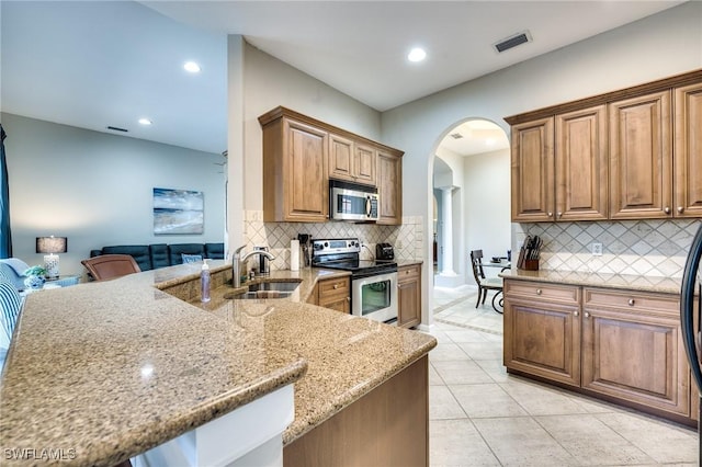 kitchen with light tile patterned flooring, sink, light stone counters, kitchen peninsula, and stainless steel appliances