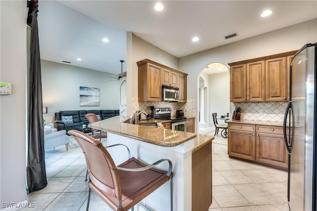 kitchen with stone counters, sink, a breakfast bar area, kitchen peninsula, and stainless steel appliances