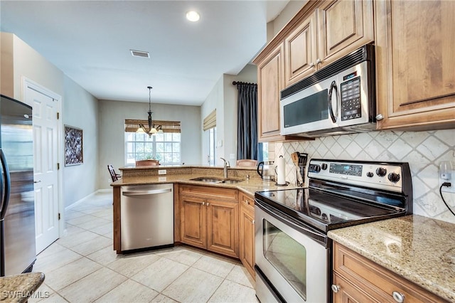 kitchen with appliances with stainless steel finishes, decorative light fixtures, light stone countertops, and sink