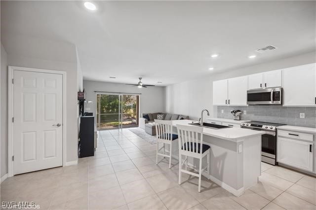 kitchen with sink, a breakfast bar, stainless steel appliances, an island with sink, and white cabinets