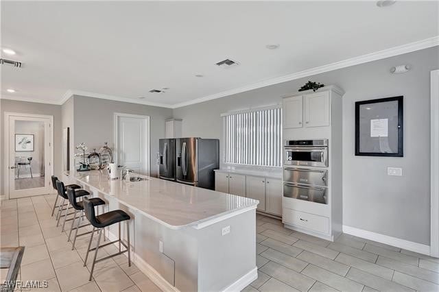 kitchen featuring crown molding, a breakfast bar, white cabinetry, stainless steel appliances, and a spacious island