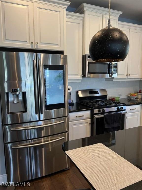 kitchen with dark wood-type flooring, backsplash, stainless steel appliances, white cabinets, and decorative light fixtures