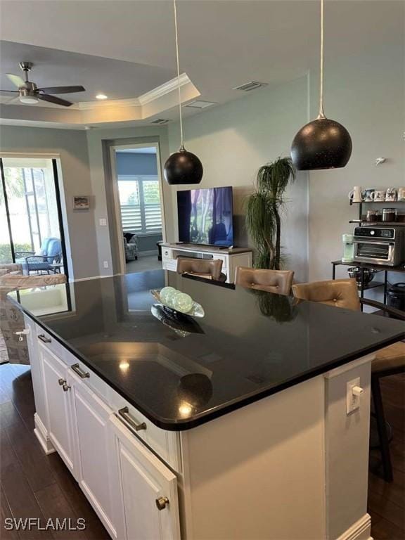 kitchen featuring dark wood-type flooring, decorative light fixtures, a raised ceiling, and white cabinets