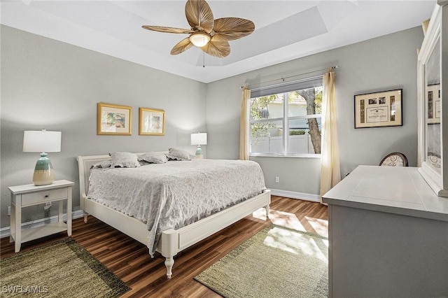 bedroom with dark wood-type flooring, ceiling fan, and a tray ceiling