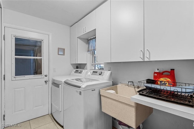 clothes washing area with cabinets, washing machine and clothes dryer, and light tile patterned floors