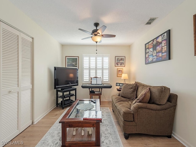 living room featuring a textured ceiling, ceiling fan, and light wood-type flooring