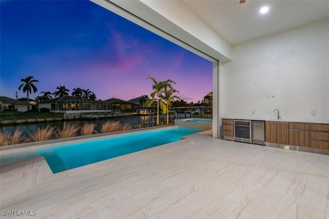 pool at dusk featuring sink and a water view