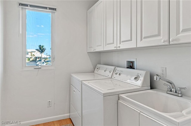 washroom featuring sink, washer and clothes dryer, light hardwood / wood-style floors, and cabinets