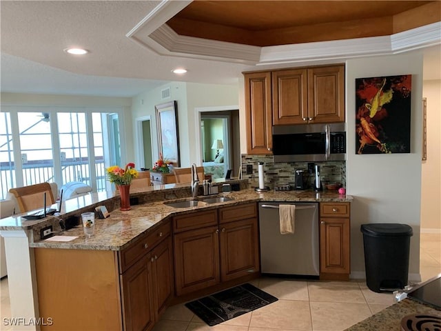 kitchen featuring sink, stainless steel appliances, tasteful backsplash, a tray ceiling, and kitchen peninsula