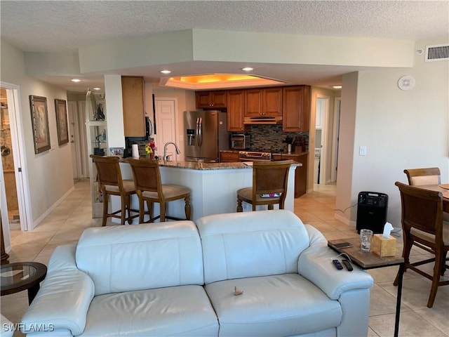 kitchen with under cabinet range hood, stainless steel appliances, a peninsula, visible vents, and brown cabinetry