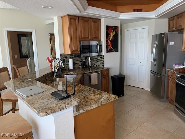 kitchen featuring a peninsula, a sink, appliances with stainless steel finishes, light stone countertops, and a raised ceiling