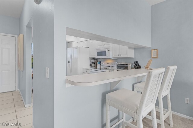 kitchen featuring white appliances, white cabinetry, a kitchen bar, a high ceiling, and light tile patterned flooring