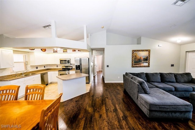 kitchen with sink, appliances with stainless steel finishes, white cabinetry, a kitchen island, and vaulted ceiling