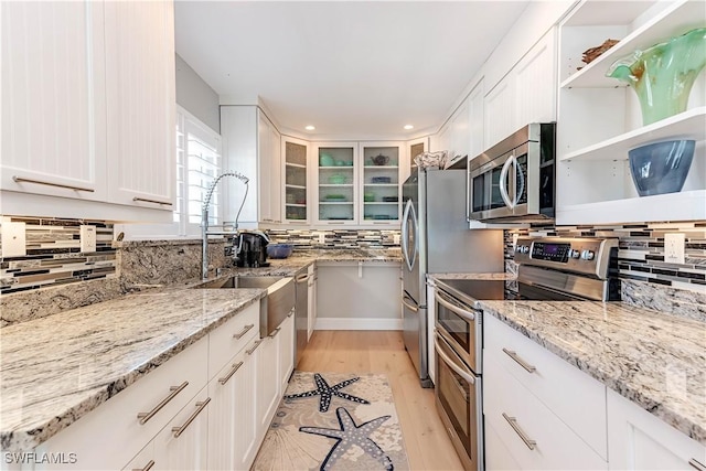 kitchen with appliances with stainless steel finishes, light stone countertops, light hardwood / wood-style flooring, and white cabinets