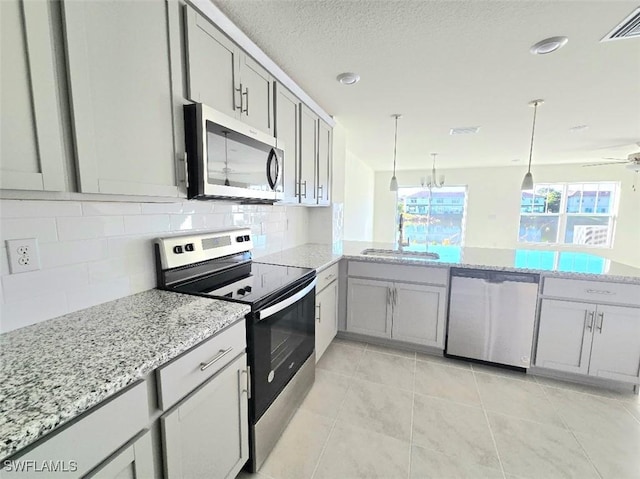 kitchen featuring sink, backsplash, hanging light fixtures, light stone counters, and stainless steel appliances