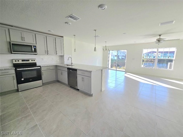 kitchen with appliances with stainless steel finishes, backsplash, light stone counters, decorative light fixtures, and kitchen peninsula