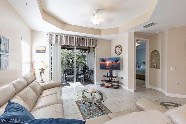 living room with a tray ceiling, ceiling fan, and light tile patterned flooring