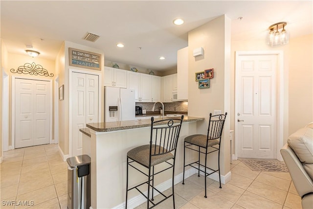 kitchen featuring dark stone countertops, a kitchen breakfast bar, kitchen peninsula, white refrigerator with ice dispenser, and white cabinets