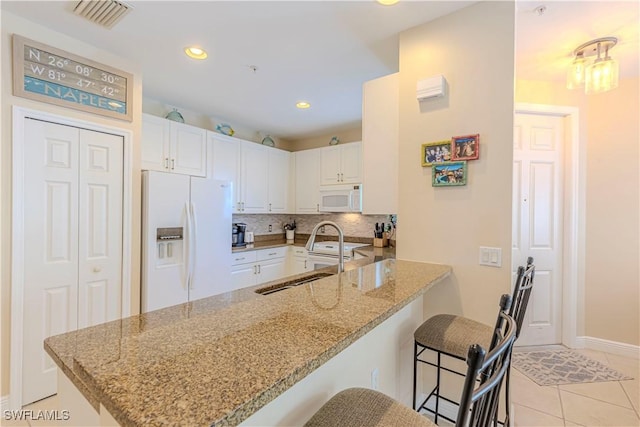 kitchen featuring white appliances, kitchen peninsula, a breakfast bar area, and white cabinets