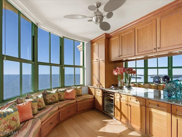 kitchen featuring light hardwood / wood-style flooring, ceiling fan, a water view, wine cooler, and light stone counters