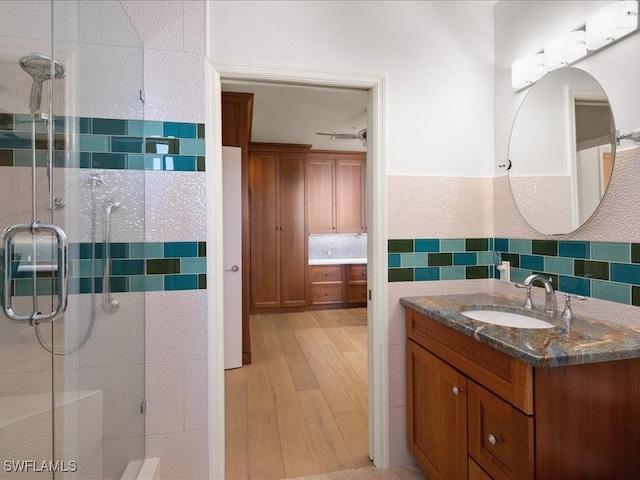 bathroom with a shower with door, vanity, wood-type flooring, and backsplash