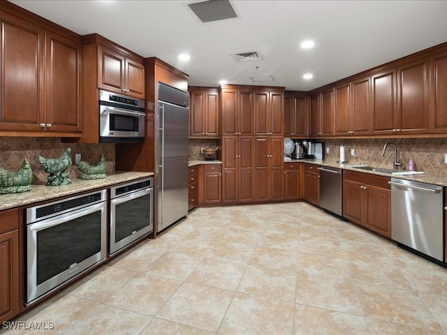 kitchen with light stone countertops, appliances with stainless steel finishes, sink, and backsplash