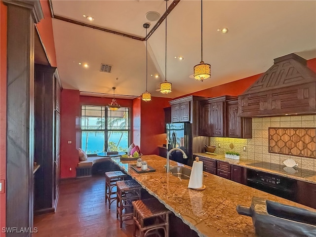 kitchen with premium range hood, a breakfast bar area, hanging light fixtures, light stone countertops, and black appliances