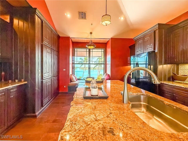 kitchen with stainless steel refrigerator, sink, light stone counters, and pendant lighting