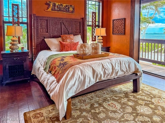 bedroom with dark wood-type flooring, access to outside, and a water view