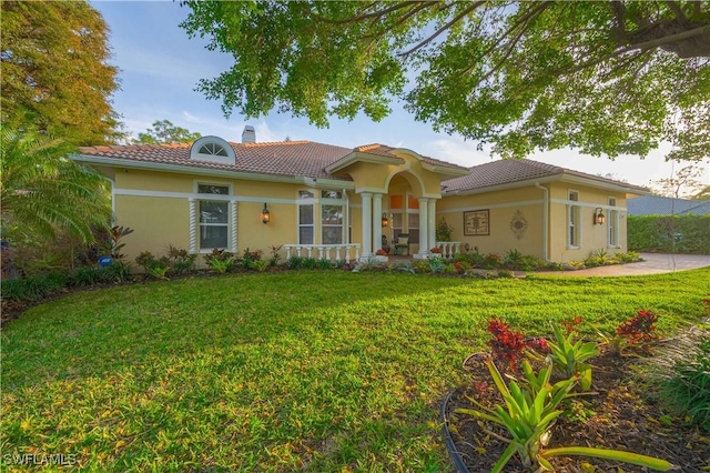 mediterranean / spanish-style home featuring a tile roof, a chimney, a front lawn, and stucco siding