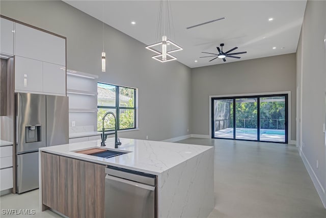 kitchen with appliances with stainless steel finishes, pendant lighting, an island with sink, sink, and white cabinets