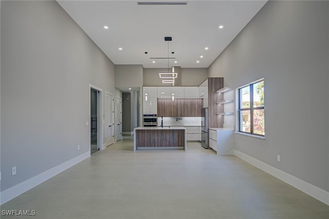 kitchen with pendant lighting, sink, appliances with stainless steel finishes, a towering ceiling, and a center island