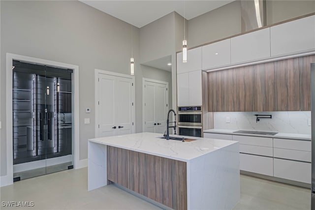 kitchen featuring sink, hanging light fixtures, a towering ceiling, white cabinets, and a center island with sink