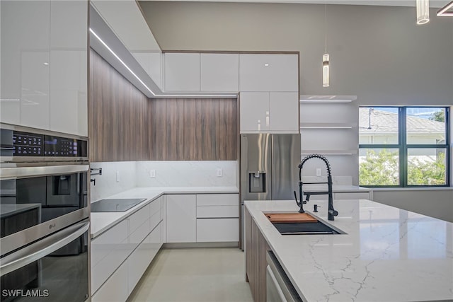 kitchen featuring sink, appliances with stainless steel finishes, light stone counters, white cabinets, and decorative light fixtures