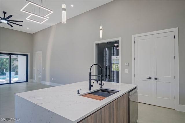 kitchen with sink, hanging light fixtures, stainless steel dishwasher, a kitchen island with sink, and a high ceiling